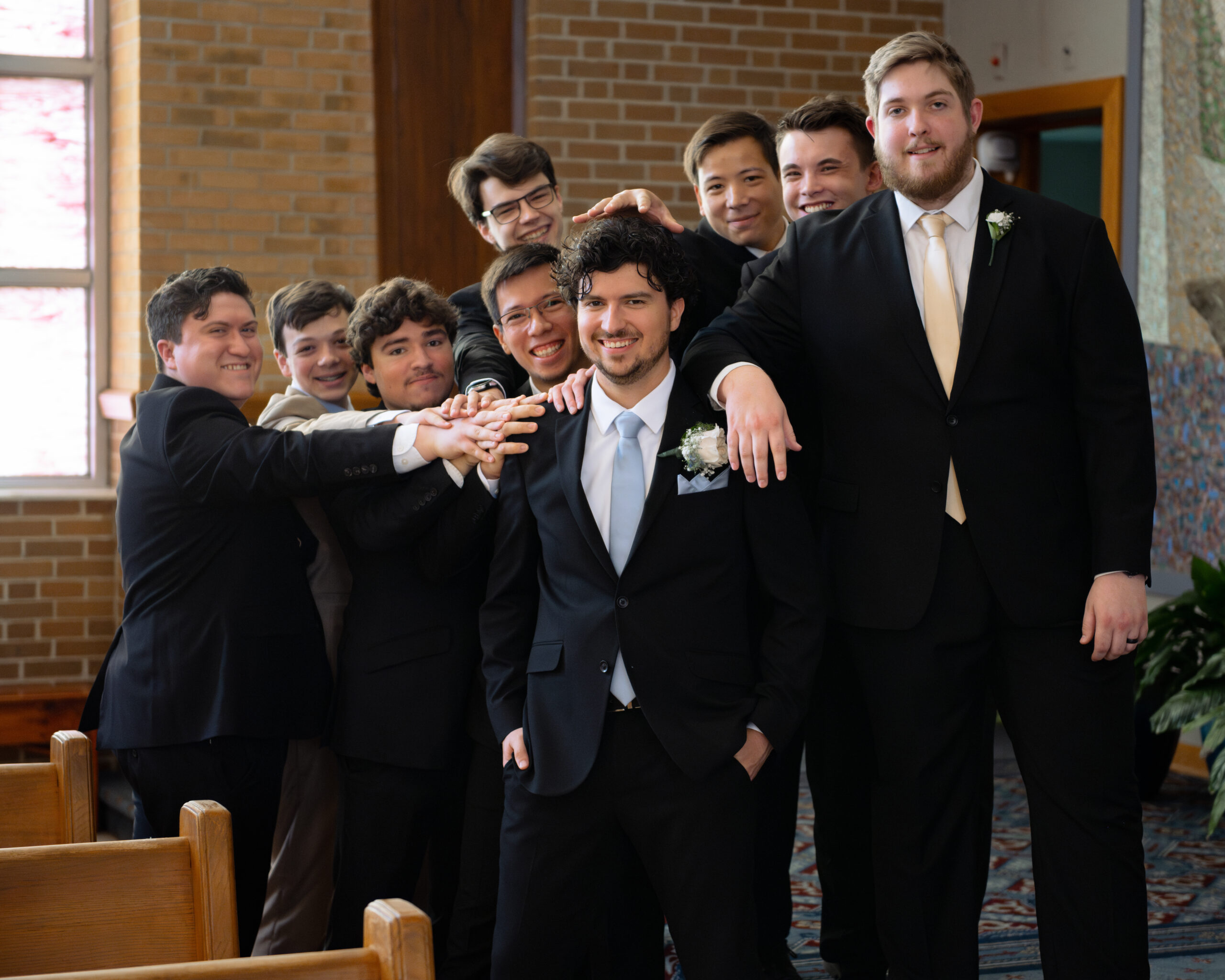 Groomsmen embrace a catholic groom at holy spirit catholic church in huntsville, alabama ahead of his wedding Mass.