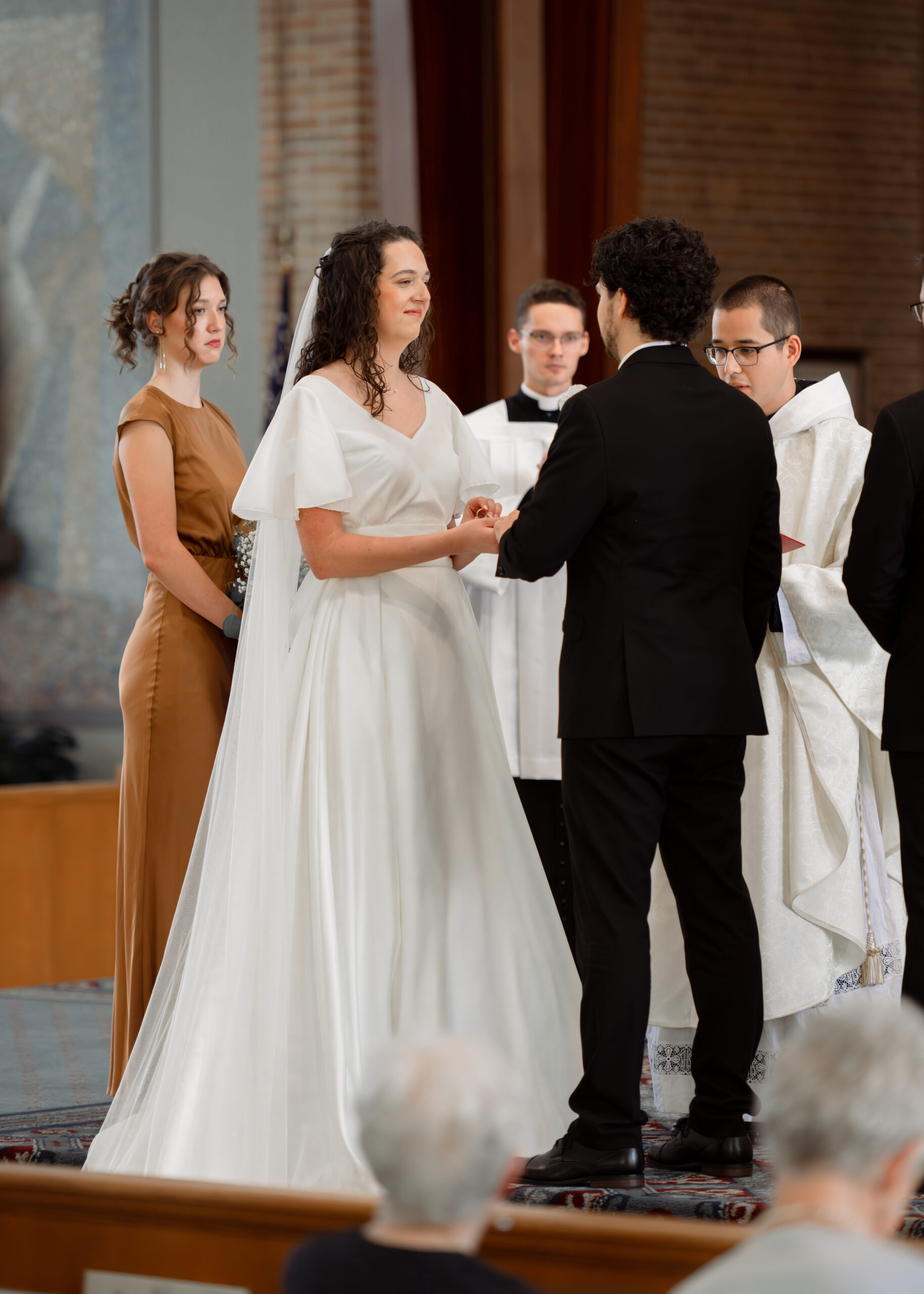 A catholic bride smiles as she places a wedding band on her groom's hand during their catholic wedding Mass in Huntsville, alabama