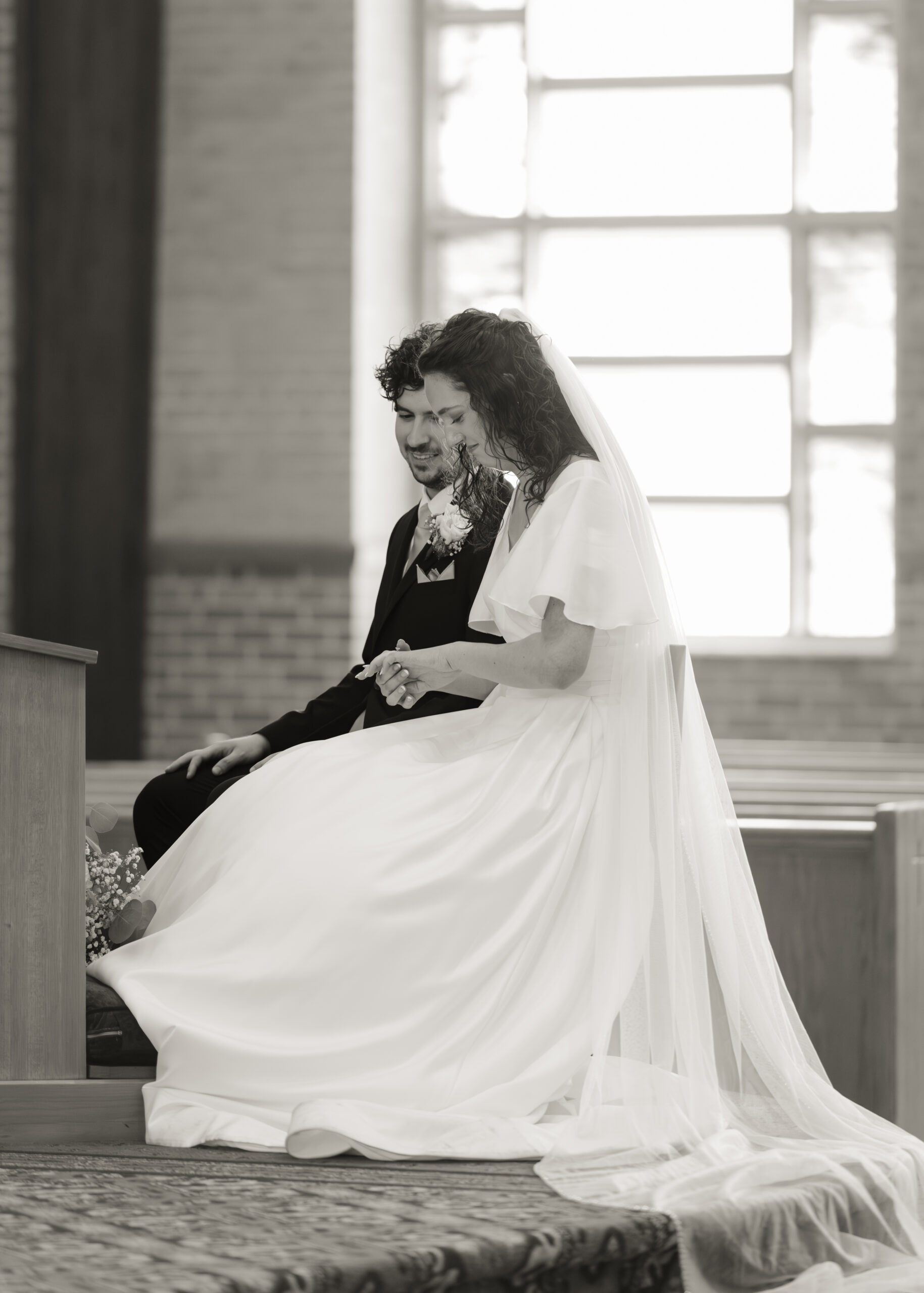 A dreamy black and white photograph shows a catholic bride and groom admiring their new wedding bands after exchanging vows during their catholic wedding Mass in huntsville, alabama