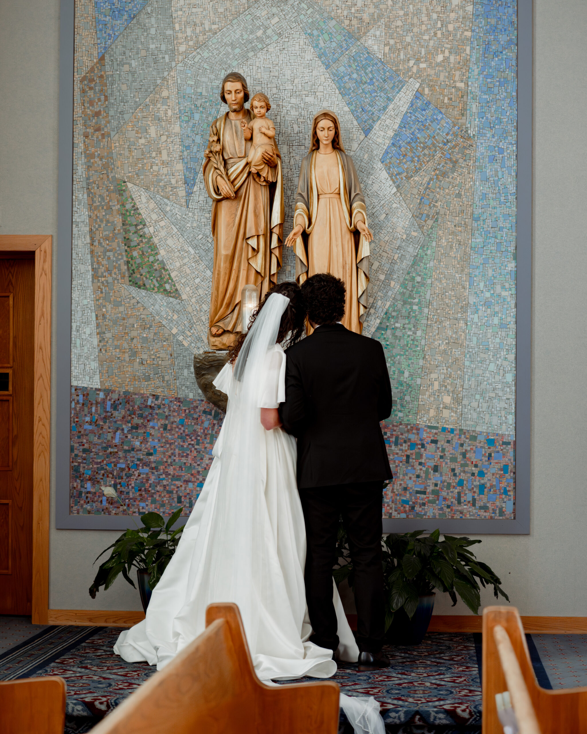 a catholic bride and groom take part in the catholic wedding tradition of presenting Mary with flowers during their catholic wedding Mass at holy spirit catholic church in huntsville, alabama