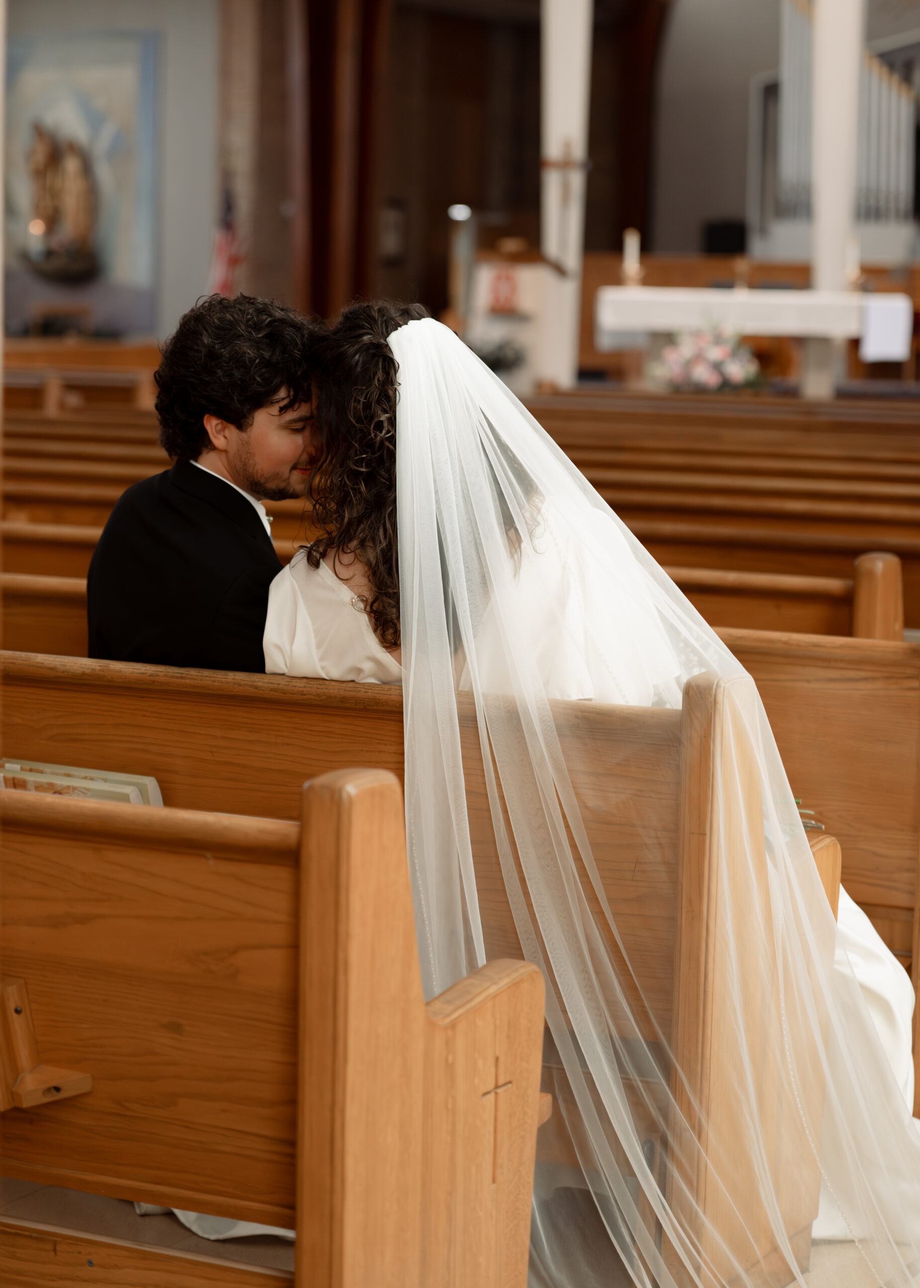 A catholic bride and groom pose for a portrait in the pews of Holy spirit catholic church in huntsville, alabama