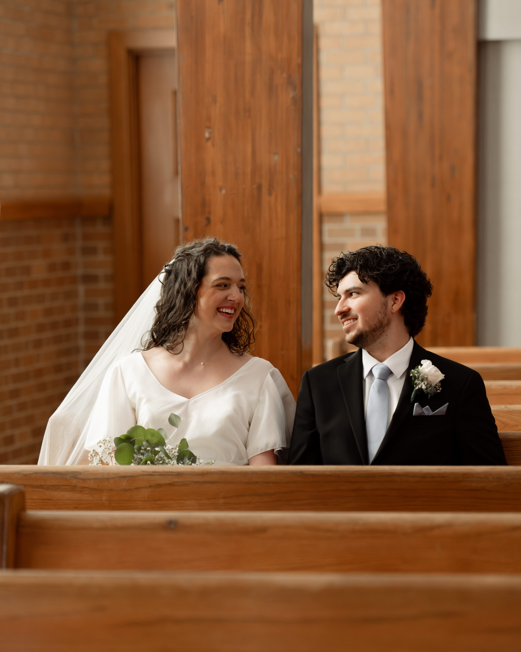 A catholic bride and groom laugh during a portrait in the pews of Holy spirit catholic church in huntsville, alabama