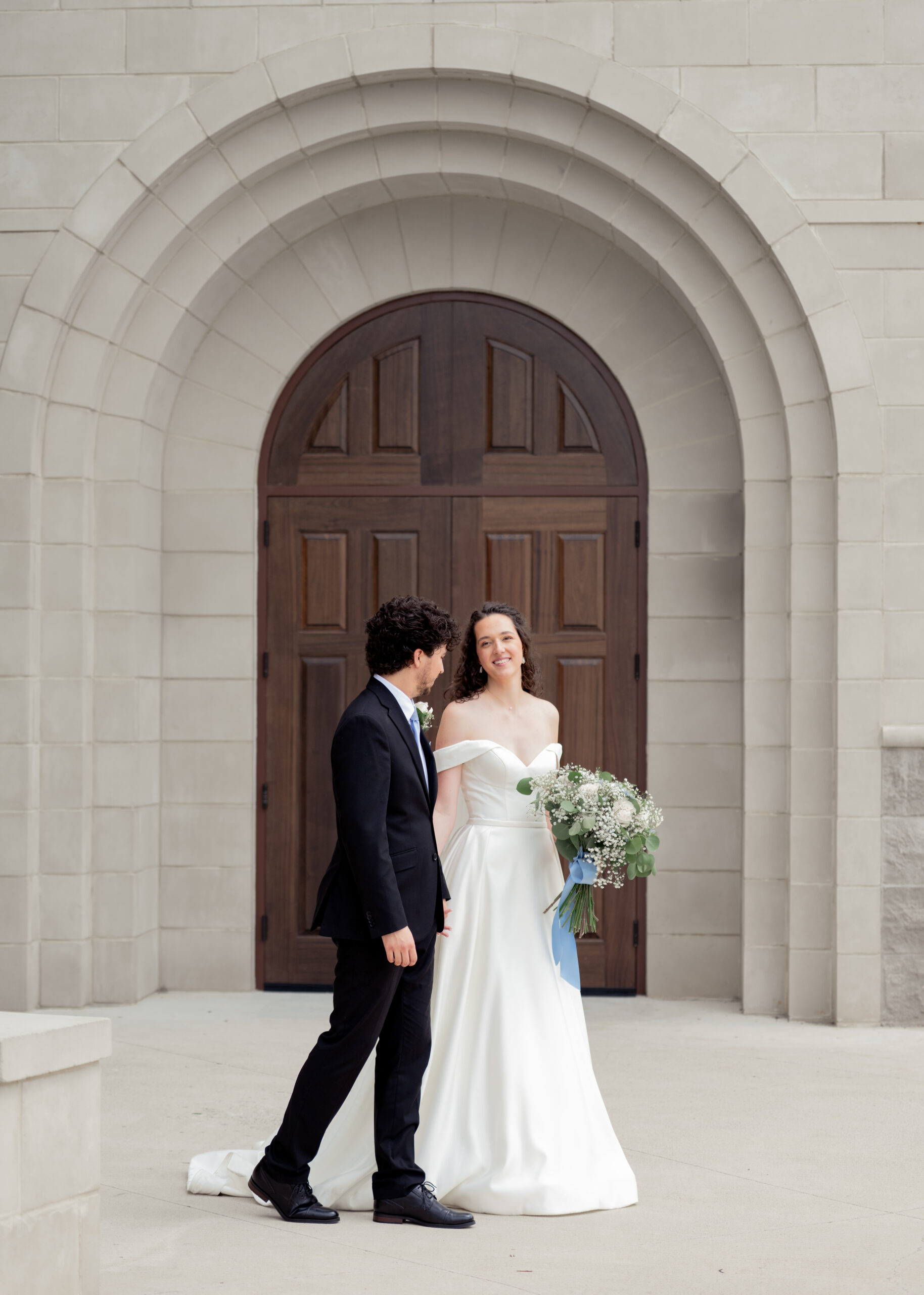 A catholic bride and groom pose for a moving portrait outside the chapel of Holy Spirit catholic church in Huntsville, Alabama