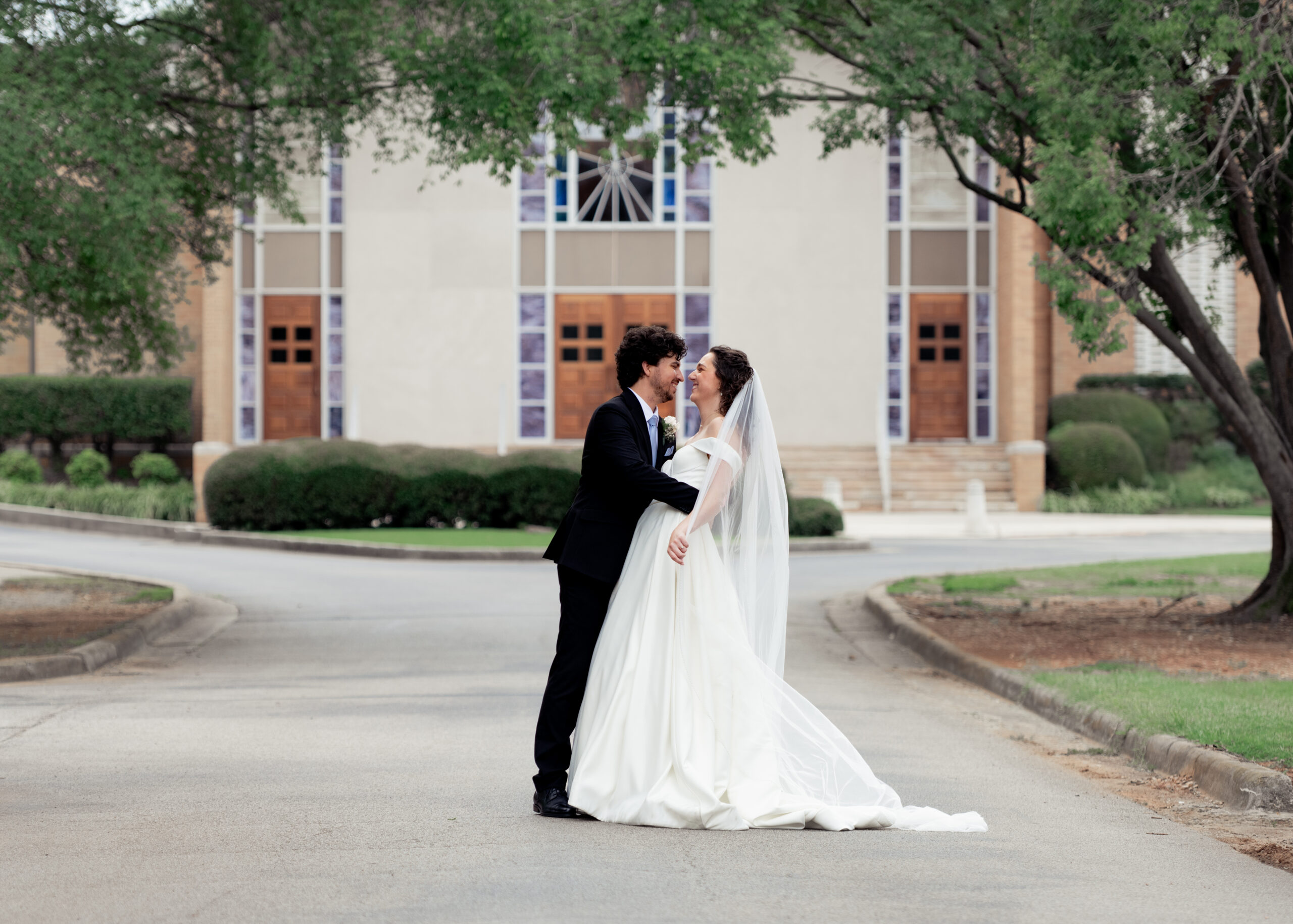 A catholic bride and groom pose for a dip outside of the catholic church where they were just married in Huntsville, Alabama