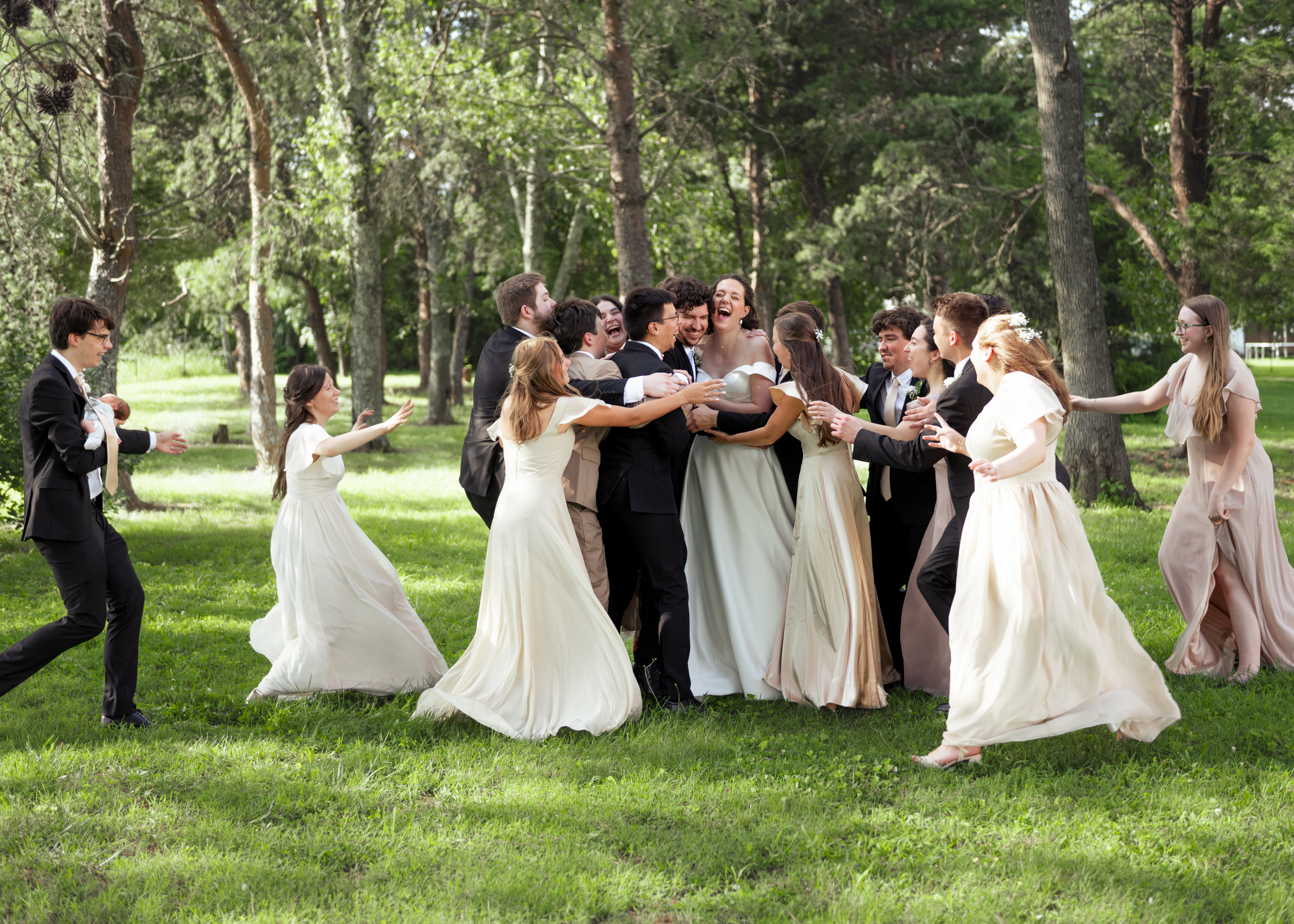 A wide angle photograph of a wedding party runs to embrace a newly married catholic couple during group photos outside of a wedding reception venue in athens, alabama