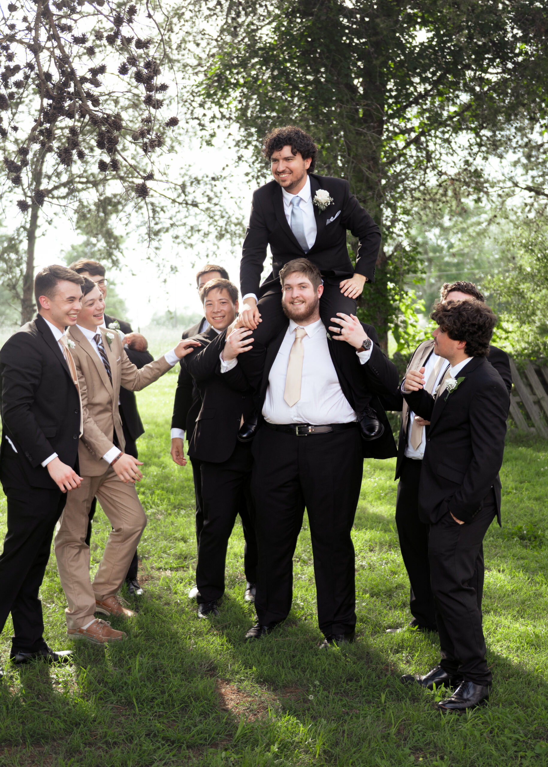 groomsmen laugh and carry a newly married groom during silly group pictures outside of a wedding reception venue in athens alabama