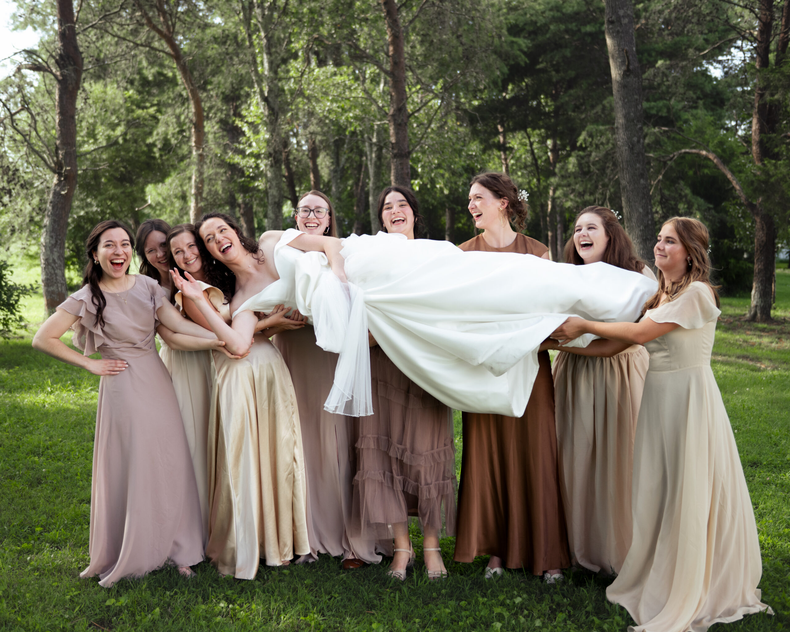Bridesmaids joyfully hold a bride during a silly group portrait after a catholic wedding Mass in athens alabama