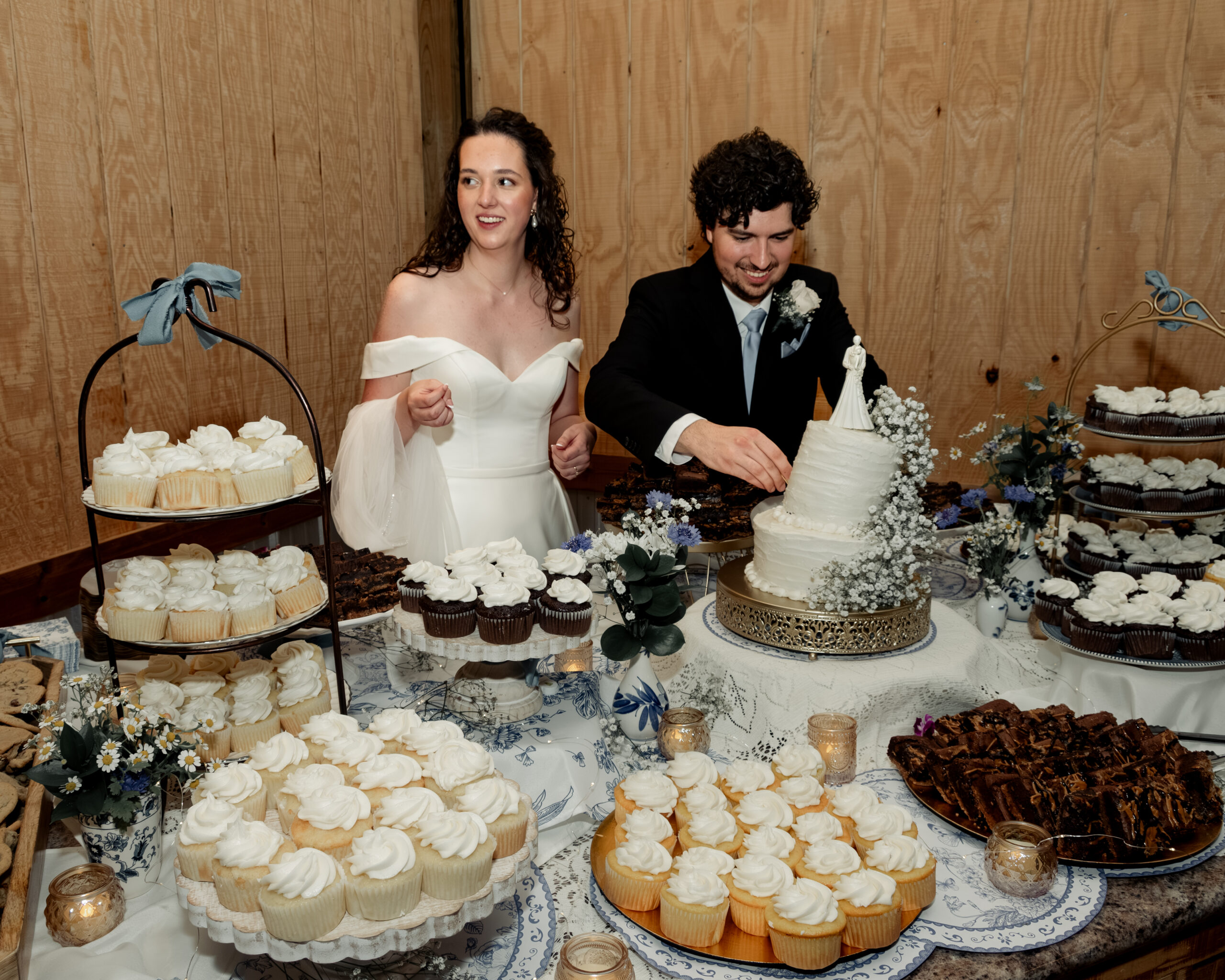 A catholic bride and groom laugh as they cut a melting wedding cake during a hot summer wedding reception in Athens Alabama
