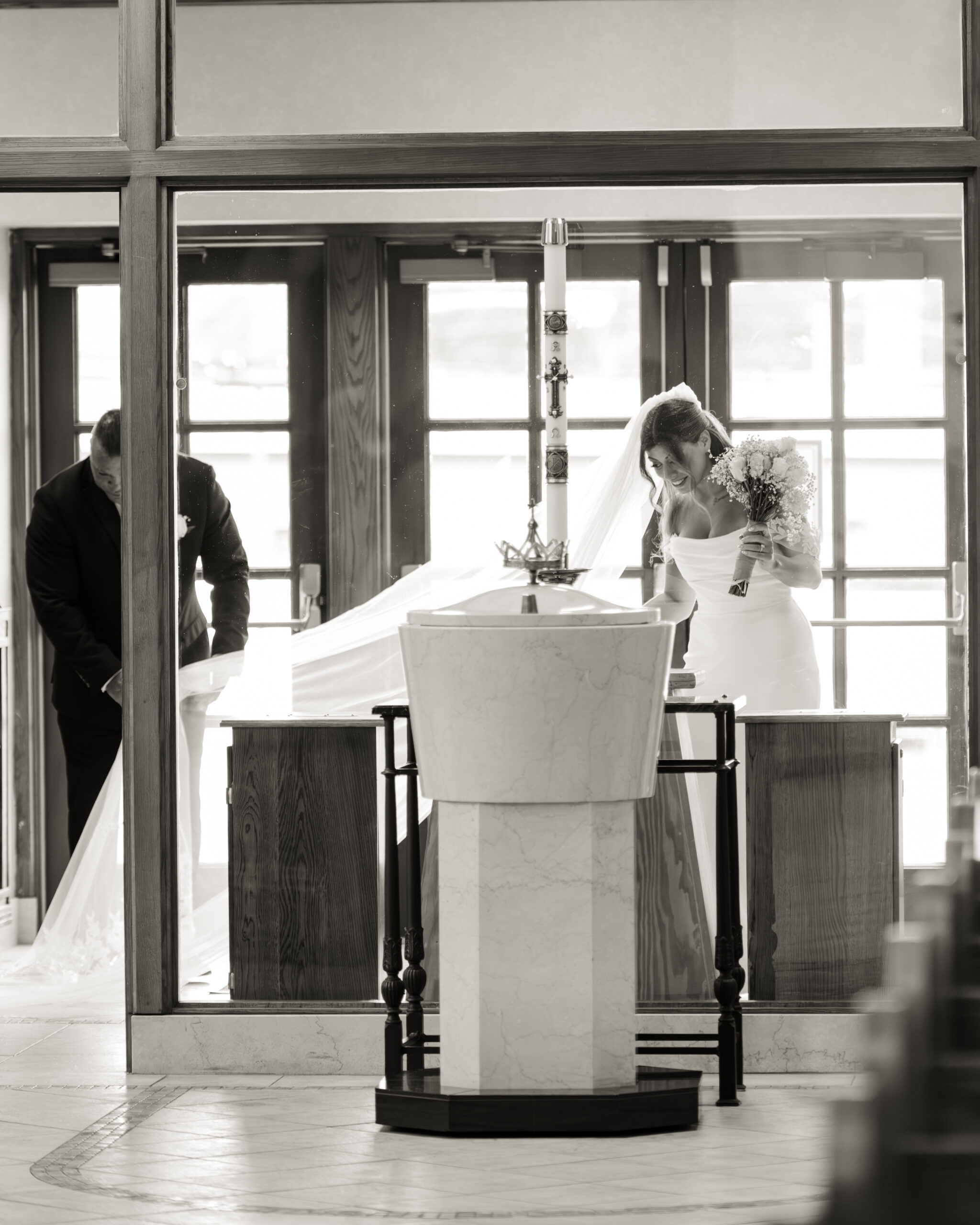 A black and white portrait of the bride laughing and adjusting her veil before she walks down the aisle during a catholic wedding ceremony at St. Ann's Catholic Church in Nashville, TN
