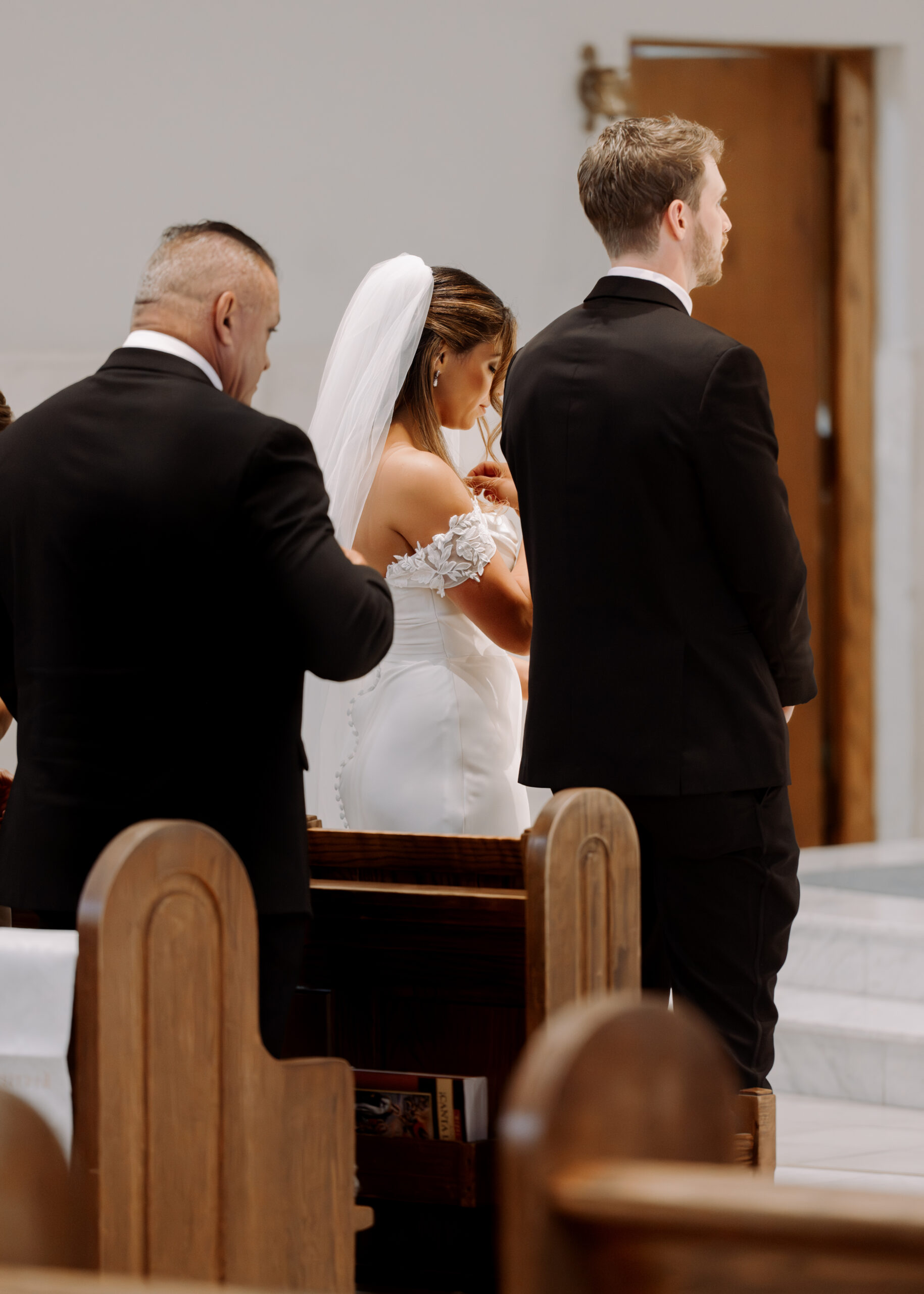 A catholic bride, illuminated by beautiful church lighting, crosses herself during a catholic wedding ceremony at St. Ann's Catholic Church in Nashville, TN