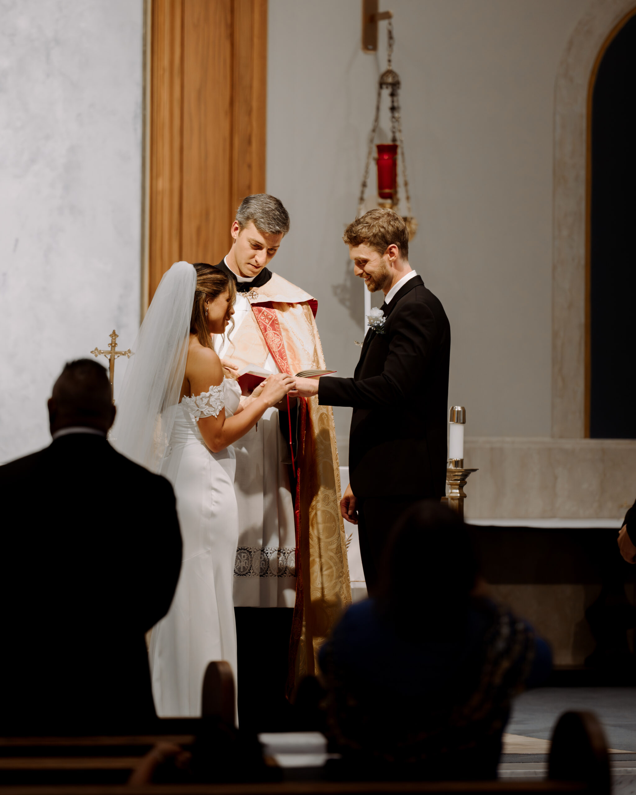 A groom laughs as his bride places his wedding band on his finger during a catholic wedding ceremony at St. Ann's Catholic Church in Nashville, TN