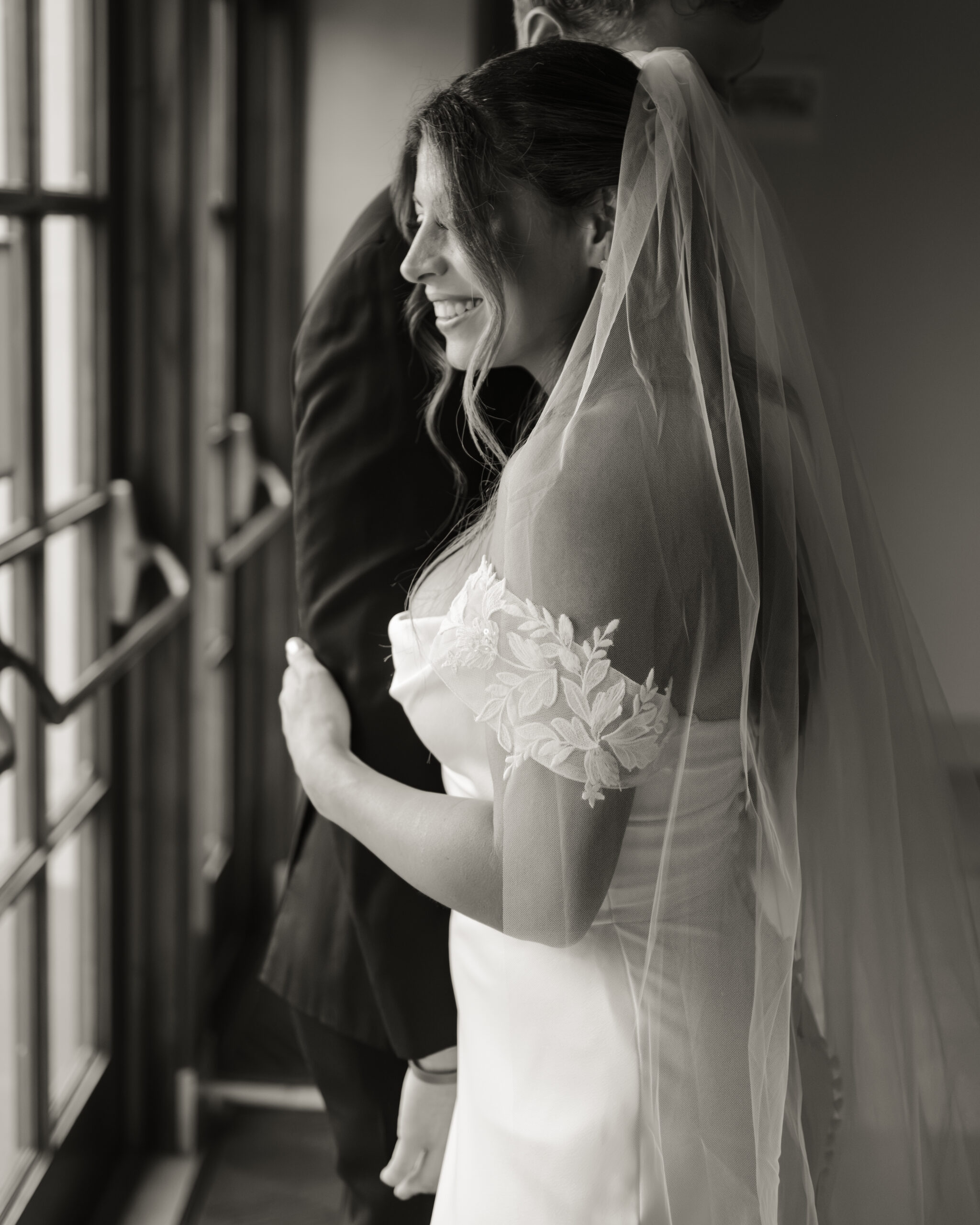 A simple black and white portrait of a bride's authentic smile while hugging her groom after their Catholic wedding ceremony at St. Ann's Catholic Church in downtown Nashville.