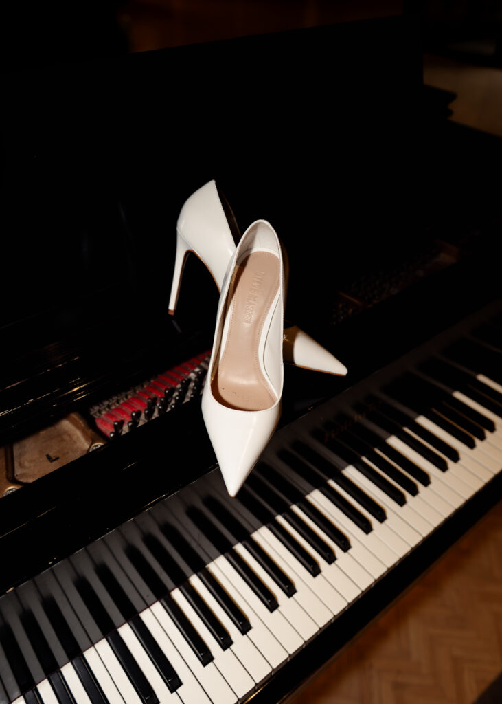 tho shoes of a nashville catholic bride sit on a piano on music row to show the classic and editorial style of the wedding and the nashville home of the bride